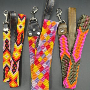 May include: Three colorful woven dog leash handles with leather accents and metal clasps. The handles feature vibrant geometric patterns in shades of red, yellow, orange, pink, purple, and green.