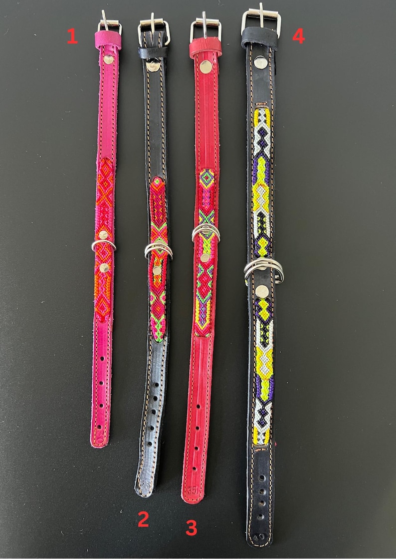 May include: Four leather dog collars in varying colors. The collars are pink, black, red, and black. Each collar has a silver buckle and a decorative beaded design in various colors. The collars are displayed on a black surface.
