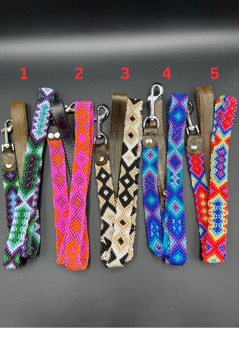 May include: A collection of six colorful dog leash handles with woven patterns. Each handle features a different design, including geometric and diamond patterns, in various colors like green, pink, blue, and red. They have brown leather accents and metal clasps.