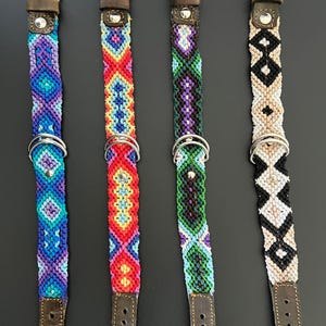 May include: Four colorful dog collars with macrame designs. Each collar features a different pattern and color scheme, including blue, red, green, and black. The collars have brown leather straps and silver metal hardware.