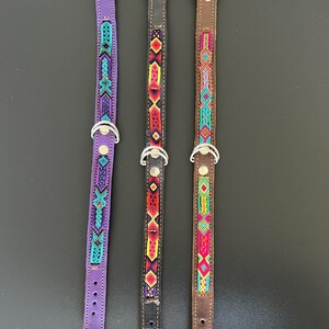 May include: Three dog collars with beaded designs. The collars are purple, black, and brown. Each collar has a silver-colored metal buckle and a D-ring. The beaded patterns feature geometric shapes in various colors, including turquoise, red, yellow, and pink.