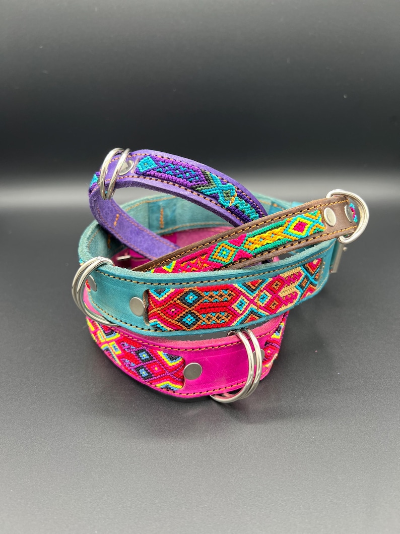 May include: Three colorful dog collars stacked on top of each other. The collars are made of leather and feature intricate woven patterns in shades of purple, teal, pink, red, and yellow. Each collar has a silver metal ring for attaching a leash.