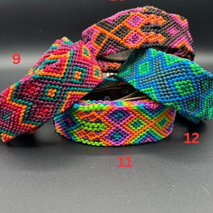 May include: A collection of colorful woven bracelets with geometric patterns. The bracelets feature a variety of colors, including pink, orange, green, and blue. The bracelets are displayed on a dark surface.