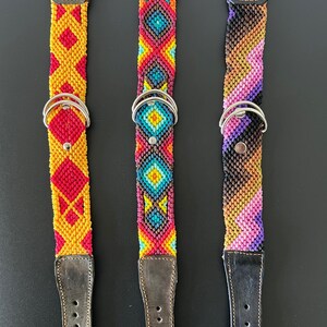 May include: Three colorful dog collars with woven patterns. The collars feature leather accents, metal hardware, and vibrant geometric designs in red, yellow, blue, and purple. Each collar has a metal D-ring for leash attachment.