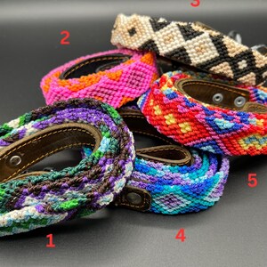 May include: A collection of colorful woven dog collars with leather backing and metal hardware. The collars feature various patterns and color combinations, including purple, blue, green, pink, red, and black and white. The collars are displayed on a dark background.