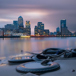 Fine Art long exposure photograph of Canary Wharf with the river Thames in the foreground, taken during the golden hour in London.