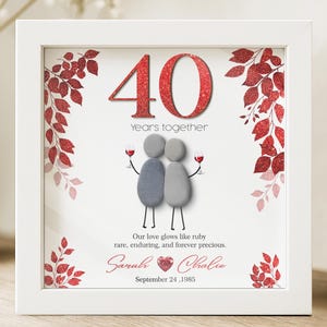 May include: A framed anniversary art piece with a white border. The artwork features the number "40" in red glitter, the words "Years together", and a couple holding wine glasses. The text reads "Our love glows like ruby rare, enduring, and forever precious."