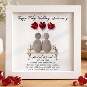 May include: A framed artwork for a ruby wedding anniversary. The white frame surrounds a picture with two pebble figures on a bench, with red heart-shaped balloons. Text reads "Happy Ruby Wedding Anniversary" and includes a date and a loving message.