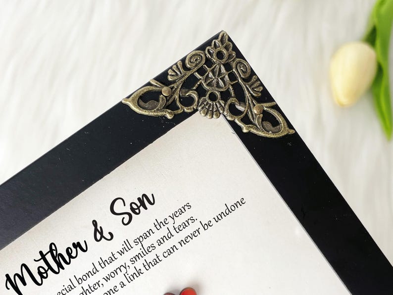 May include: A black picture frame with an ornate gold corner piece. The frame contains a white card with the text "Mother & Son" and a quote about the special bond between a mother and son.