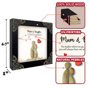May include: A framed pebble art print with a black frame and a silver-colored border. The print features a mother and daughter figure made of natural pebbles with a red heart above them. The text on the print reads "Mum & Daughter, No matter where we go, you will always have me around".