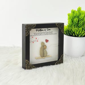 May include: A framed pebble art piece depicting a mother and son. The artwork is in a black frame with ornate gold corners. The text reads "Mother & Son" and "We have a special bond that will span the years Through the laughter, worry, smiles and fears, Mother and son: two hearts as one a link that can never be undone."