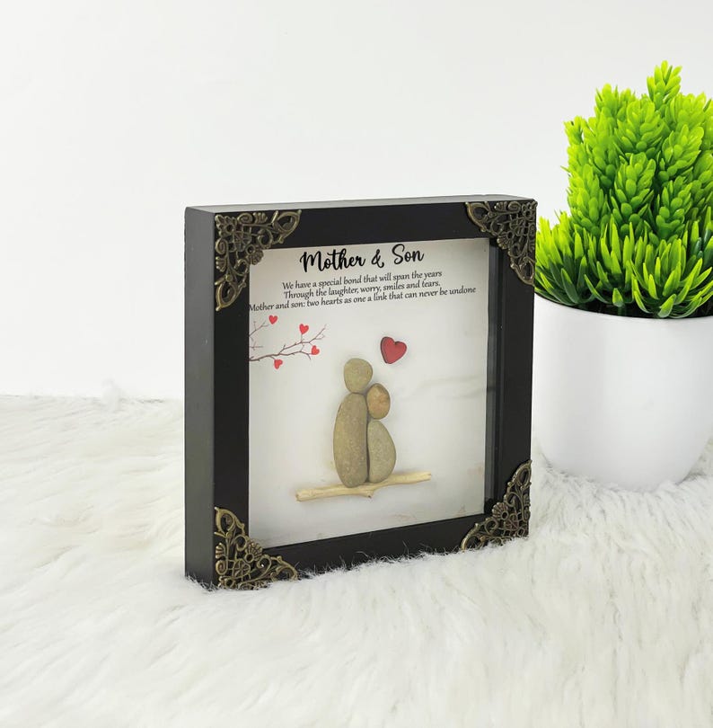 May include: A framed pebble art piece depicting a mother and son. The artwork is in a black frame with ornate gold corners. The text reads "Mother & Son" and "We have a special bond that will span the years Through the laughter, worry, smiles and fears, Mother and son: two hearts as one a link that can never be undone."