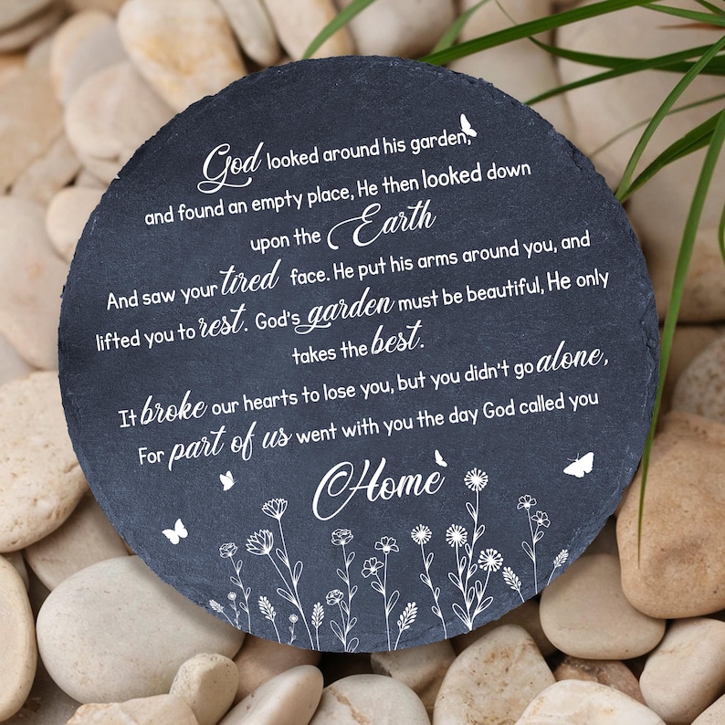 May include: A round, dark gray memorial stone with white text. The inscription includes the words "God," "Earth," and "Home," along with a poem about loss. Delicate floral and butterfly designs are also present.