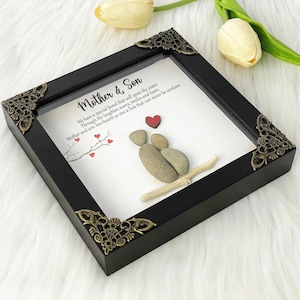 May include: A framed artwork featuring a pebble art design of two figures holding hands, representing a mother and son. The artwork is set against a white background with a quote that reads: "We have a special bond that will span the years. Through the laughter, worry, smiles and tears. Mother and son, two hearts as one, a link that can never be undone."