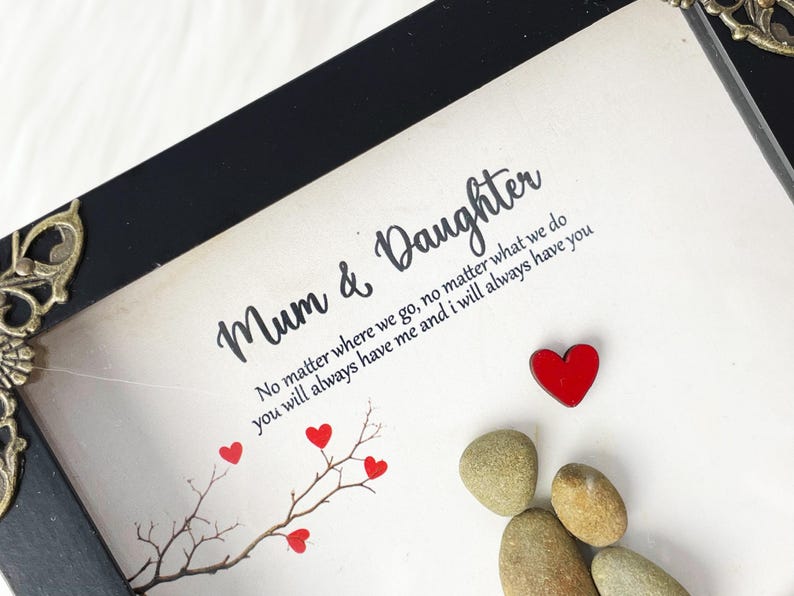 Puede incluir: Una impresi&oacute;n enmarcada con un marco negro y un fondo blanco. La impresi&oacute;n presenta una cita sobre el v&iacute;nculo entre una madre y una hija, junto con un peque&ntilde;o &aacute;rbol con corazones rojos y un grupo de piedras grises. La cita dice: "Mam&aacute; e Hija No importa a d&oacute;nde vayamos, no importa lo que hagamos, siempre me tendr&aacute;s y yo siempre te tendr&eacute;."