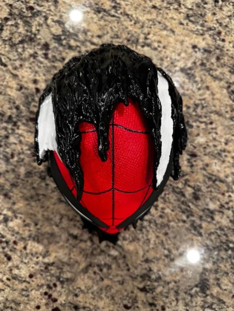 May include: A red and black Spider-Man mask with black dripping paint on the top and white accents on the sides.