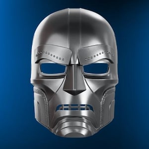 May include: A silver-coloured mask with a unique design, including eye openings, a prominent nose piece, and a mouth area with horizontal slits. The mask has a smooth, reflective surface against a blue background.