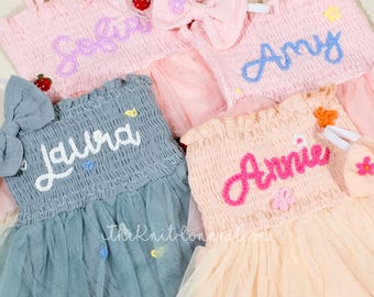May include: Four tulle dresses with embroidered names, Sofia, Laura, Amy, and Annie. Each dress has a different color and features a small bow or flower embellishment.