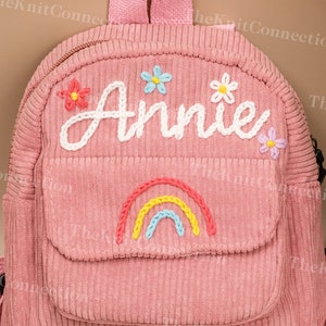May include: Pink corduroy mini backpack with a rainbow and flower embroidery. The backpack is personalized with the name "Annie".