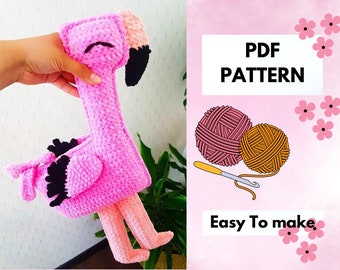 May include: A pink crocheted flamingo plush toy with black accents on the wings and beak. The flamingo is held up in front of a white background with a sign that says "PDF PATTERN" and "Easy To make."