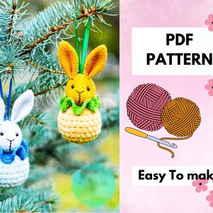 May include: Two crocheted bunny ornaments, one yellow and one white, hanging from a pine tree branch. The image also includes a pink and orange ball of yarn, a crochet hook, and the text "PDF PATTERN Easy To Make."