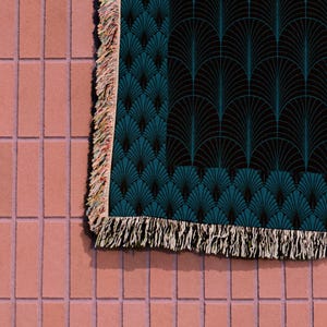 May include: A teal and black throw blanket with a geometric pattern of overlapping fan shapes. The blanket has a fringe border.
