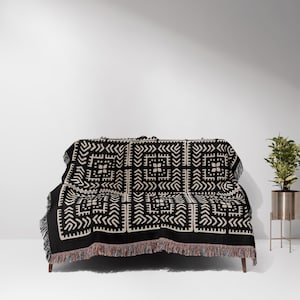 May include: A black and white woven throw blanket with a geometric pattern. The blanket is draped over a couch with black legs.
