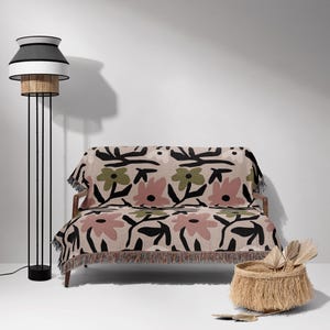 May include: A contemporary living room setting with a floral patterned throw blanket on a wooden sofa. A black and white floor lamp is on the left, and a woven basket with decorative items is on the floor.