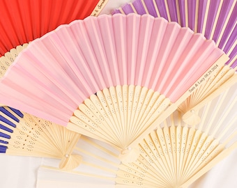 May include: A set of four hand fans with wooden handles and fabric panels. The fans are in various colors, including red, pink, purple, and white. The pink fan has the text "Sam & Lucy 08.29.2024" printed on it.