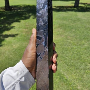 May include: A tall, polished stone tower with a hexagonal base and a pointed top. The stone features a dark, mottled pattern with deep black, charcoal gray, and subtle blue-toned inclusions throughout its smooth, reflective, and faceted surface.