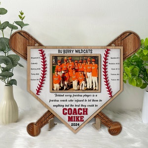 Puede incluir: Un marco de madera con forma de bate de béisbol con una foto de un equipo de béisbol juvenil. El marco tiene el texto "8U BERRY WILDCATS" y una lista de nombres y números de jugadores. El texto "Behind every fearless player is a fearless coach who refused to let them be anything but the best they could be COACH MIKE 2024" está impreso en el marco.