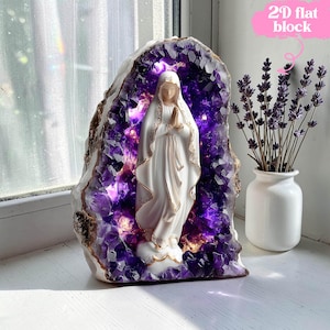 May include: A white statue of a religious figure with hands clasped in prayer, set within a large, illuminated amethyst geode. The geode is surrounded by a gold-colored border. A small white vase with lavender stems is to the right.