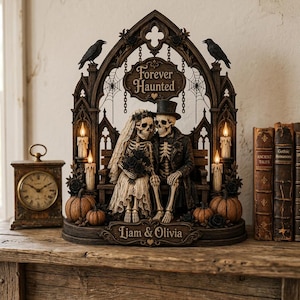 May include: A decorative figurine featuring two skeletons dressed as a bride and groom sitting on a bench under a gothic arch. The arch displays the text Forever Haunted and the base is inscribed with Liam & Olivia, accented by pumpkins and candles.