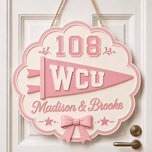 May include: A scalloped, cream-colored wooden door sign featuring the number 108, a pink pennant with the letters WCU, and the names Madison & Brooke in pink script. The sign is accented with two pink stars and a pink bow at the bottom.