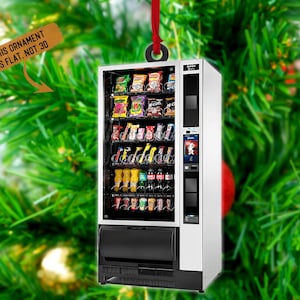 May include: A silver vending machine ornament with a red ribbon. The vending machine is filled with various snacks and drinks. The ornament is labeled "This ornament is flat, not 3D".