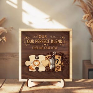 Op de afbeelding: Houten bord met de tekst "OUR PERFECT BLEND FUELING OUR LOVE". Het bord toont puzzelstukjes met koffiethema's, waaronder een koffiekopje, een hart, een koffiezetapparaat en koffiebonen. Het bord wordt op een houten standaard weergegeven.