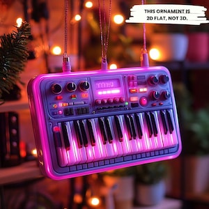 May include: A 2D flat, not 3D, ornament shaped like a synthesizer keyboard. The ornament has a purple and pink color scheme with a glowing pink border and keys. The text "THIS ORNAMENT IS 2D FLAT, NOT 3D" is visible.