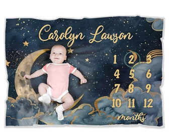 May include: A baby blanket with a navy blue background and gold stars. The blanket features a crescent moon with a gold outline and a heart in the center. The text "Carolyn Lawson" is written in gold cursive script. The blanket also has a number chart for tracking a baby's growth, with numbers 1 through 12 in gold.