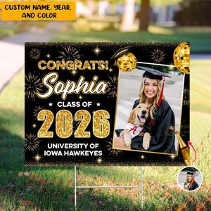 May include: A graduation yard sign with a black and gold design. The sign says "Congrats! Sophia Class of 2026 University of Iowa Hawkeyes." A photo of a graduate and dog is included. The sign is displayed on a metal stake.
