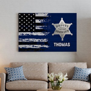 May include: A blue and white American flag with a thin blue line overlay. The flag is distressed and has a silver sheriff's star with the text "DEPUTY SHERIFF" and the name "THOMAS" below it.