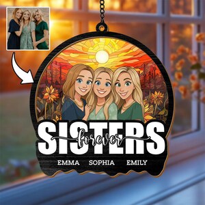 Pode incluir: Um ornamento redondo de madeira com uma ilustração de desenho animado de três mulheres e o texto "Sisters Forever". O fundo retrata um pôr do sol. Os nomes Emma, Sophia e Emily estão abaixo. Uma pequena foto das mulheres está no canto superior esquerdo.