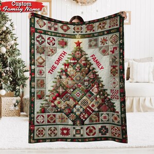 May include: A personalized Christmas quilt featuring a tree design with ornaments and the text "THE SMITH FAMILY" in red. The quilt has a patchwork design with red, green, and cream-colored squares and a dark green border.
