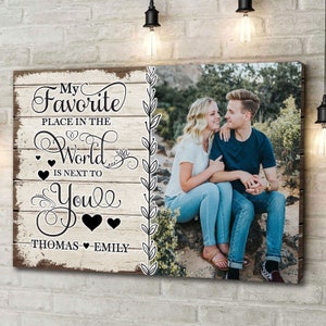 May include: A rustic wooden sign with the text "My Favorite Place in the World is Next to You" with the names "Thomas" and "Emily" at the bottom. A couple is pictured in the background.
