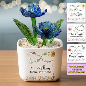 Op de afbeelding: Een witte keramische bloempot met blauwe glazen bloemen en groene bladeren. De pot is versierd met bloemmotieven en de tekst "First My Mom Forever My Friend". Extra kaarten tonen vergelijkbare ontwerpen met verschillende namen en citaten.