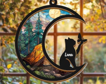 Può includere: Decorazione nera a forma di mezzaluna con una scena di campeggio e una silhouette di gatto. La scena all'interno della mezzaluna presenta una tenda, alberi e una luna piena. Una farfalla è sulla zampa del gatto e il nome "Luna" è scritto sul gatto.
