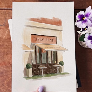 May include: A watercolor painting on paper depicting a restaurant storefront with a beige facade, dark brown window frames, and a tan awning. The text "RESTAURANT" is printed above the entrance. Two small tables with chairs are placed outside.