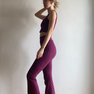 May include: A woman is wearing a maroon crop top and matching flared pants. The outfit is made of a soft, stretchy fabric.