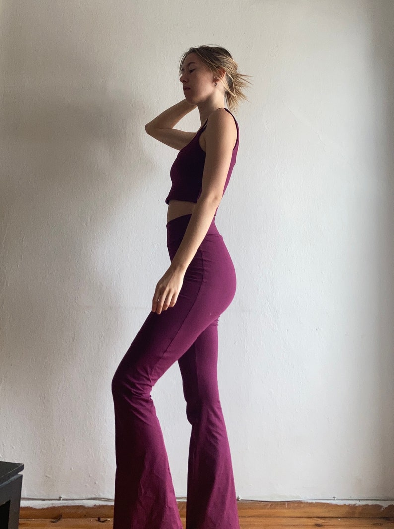 May include: A woman is wearing a maroon crop top and matching flared pants. The outfit is made of a soft, stretchy fabric.