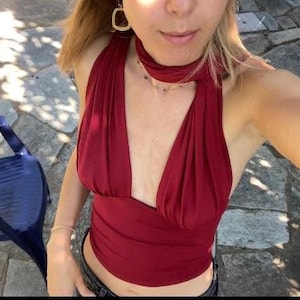 May include: A deep red halter top with a plunging neckline and a matching neck tie. The top is made of a soft, draping fabric. A dark blue plastic chair is visible in the background.