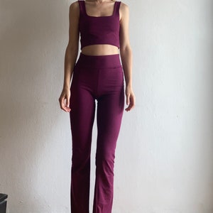 May include: A two-piece outfit in a deep purple color. The top is a sleeveless crop top with a square neckline. The pants are a high-waisted, wide-leg style.